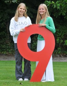 Two pupils celebrating fantastic GCSE results pose with a giant number 9 cardboard cut-out