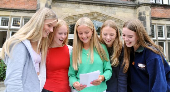 Pupils surrounded by their friends opening their GCSE results