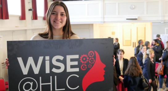 Samy Crawford, a former pupil studying a Masters degree in Aerospace Engineering holding the WISE@hlc banner